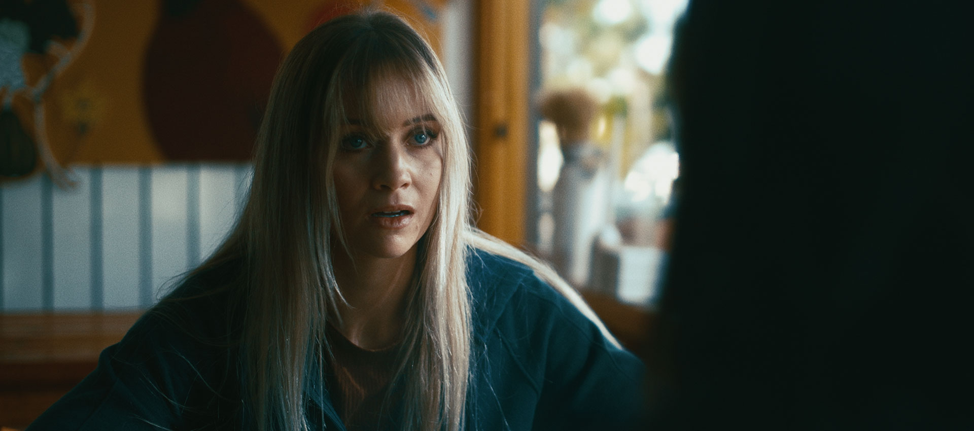 A woman faces another person in a warmly lit room in Another